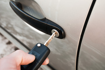 A hand is holding a car's remote control pointing to the door.a man opens a machine.