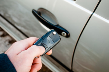 A hand is holding a car's remote control pointing to the door.a man opens a machine.
