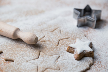 Cookies stars cut out of the dough preparation before baking along with prepared biscuits, rolling pin and cutter.