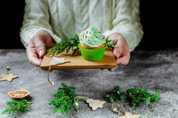 Female hands hold a homemade cream muffin. Traditional christmas dessert on gray concrete background