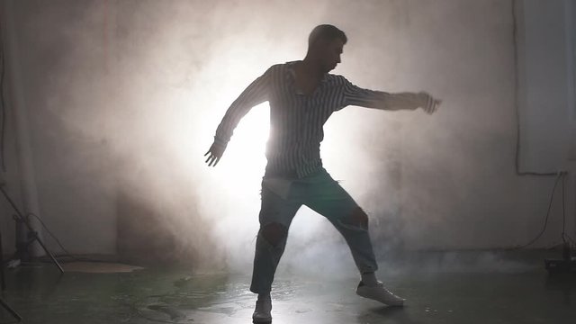 Slow motion silhouette of vigorous dancer male dancing street dance, jump in the air isolated over smoky background