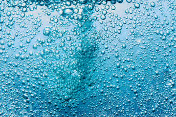Sparkling Mineral Water Background. Blue bubbles of fresh soda float to the surface of drink to...