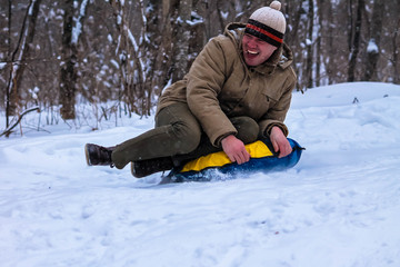 Fototapeta na wymiar Cheerful guy rolls down the hill on snow tubing in the woods . Sledding. Winter entertainment. 