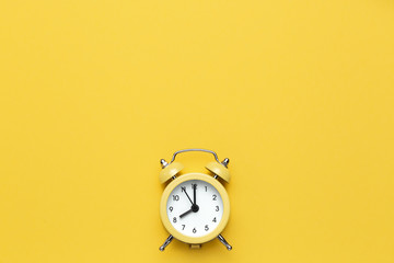Yellow round alarm clock on the yellow background. - obrazy, fototapety, plakaty