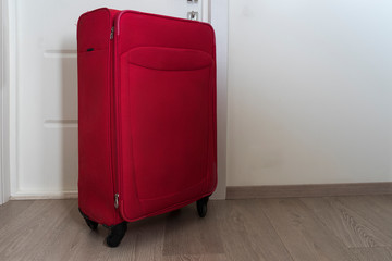 A large red suitcase stands near the door. The concept of a summer vacation. the suitcase is ready for travel