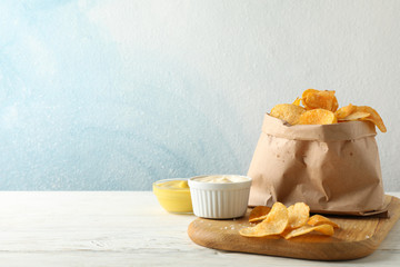 Paper bag of potato chips. Beer snacks, sauce on cutting board, on white wooden background, space for text