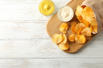 Paper bag of potato chips. Beer snacks, sauce on cutting board, on white wooden background, space for text. Top view