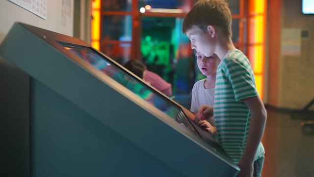 Two schoolchildren are standing near a large touch screen. Online education. Adaptation of life to the virus COVID-19