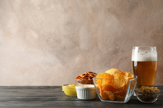 Beer snacks, glass of beer, potato chips, beer nuts, sauces, glass of beer on wooden background, space for text