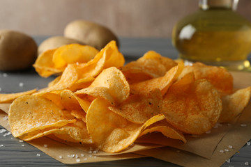 Potato crispy chips on craft paper, sault, oliv oil, potato on gray wooden background, space for text. Closeup