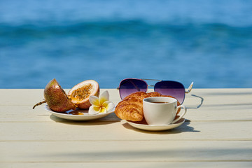 Coffee cup with croissant and fruit on the terrace and sea view on a sunny day. Concept for vacation, vacation or summertime.