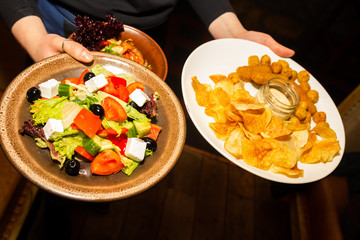 Waiter hands holding plates with potato chips, snaks, and salad with feta.