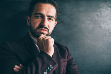 Portrait of handsome caucasian businessman in formal outfit pondering on idea for project feeling confident, serious successful male entrepreneur dressed in luxury clothes looking at camera near wall