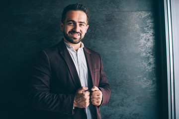 Portrait  caucasian male entrepreneur in trendy stylish outfit standing indoors enjoying luxury lifestyle, successful businessman dressed in stylish clothes posing near promotional background.