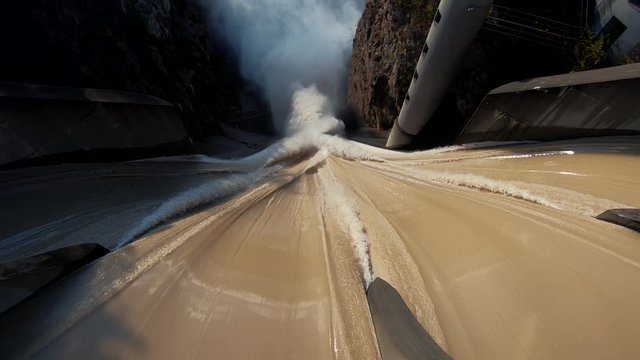 Slow motion tilt down dirty brown flooded river water flows over concrete spillway
