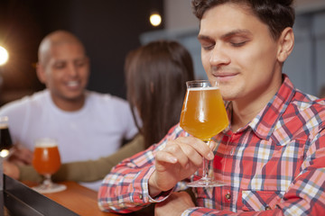 Cropped shot of a handsome young man enjoying aroma of delicious beer in his glass. Happy man having beer at the pub