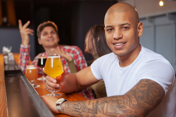Handsome African man smiling to the camera, holding beer glass, relaxing at the pub