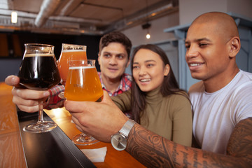 Diverse group of friends clinking beer glasses. Selective focus on beer glasses in the hands of young people celebrating at the bar
