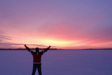 Fototapeta premium A man with wide outstretched arms in twilight, stands back to the camera on the snowy surface of the frozen lake