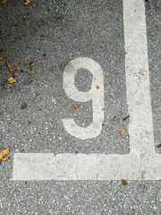 Number 9 written on street asphalt as a parking lot place for a car with leaves and street dirt around in an urban setting