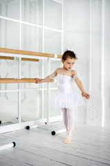 Fototapeta na wymiar Classic ballet dancer child posing at barre on rehearsal room background. 6 years old girl in white ballet clothes with mirrors on background. Training session