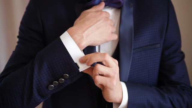 Young elegant man in a blue suit straightens cufflinks on a shirt. The morning of the groom.