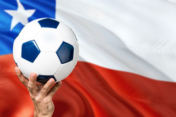 Chile soccer concept. National team player hand holding soccer ball with country flag background. Copy space for text.