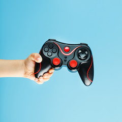 A gamepad on a blue background holds a child's hand as a weapon. Minimalistic creative concept of the younger generation of gamers.