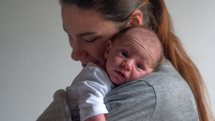 Authentic shot of neo mother is keeping in arms and caressing her newborn baby in a nursery in a morning. 