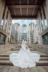 Fototapeta premium portrait of a beautiful bride in long dress and viel on the background of a business center