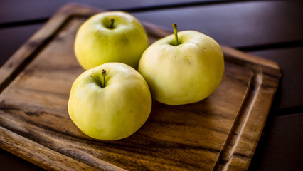 Three green organic healthy apples on wooden board.