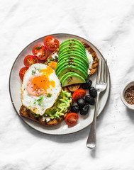 Delicious brunch - fried egg, avocado, grilled bread, dried olives, cherry tomatoes. Delicious healthy breakfast, snack on a light background, top view