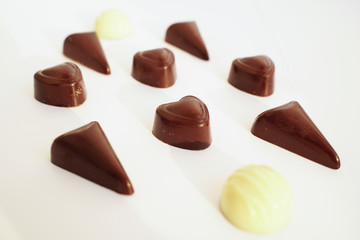 Tasty candies from dark and white chocolate isolated on white background macro. Candy from black chocolate is heart-shaped.
