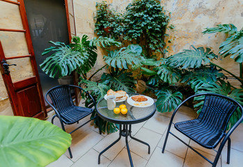 Breakfast plates on table of small green courtyard of historical house in Mediterranian region. Romantic holidays concept