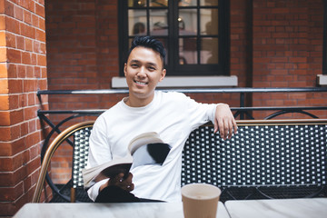 Young man reading funny book in cafe