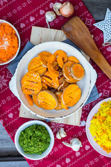 Grilled baked pumpkin slices in pan on red Christmas tablecloth background.