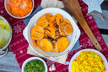 Grilled baked pumpkin slices in pan on red Christmas tablecloth background.