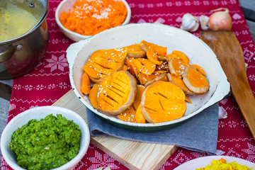 Grilled baked pumpkin slices in pan on red Christmas tablecloth background.