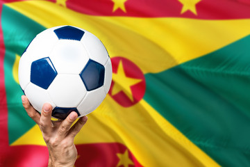 Naklejka premium Grenada soccer concept. National team player hand holding soccer ball with country flag background. Copy space for text.