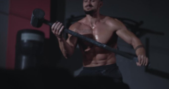 Concentrated strong athletic man lift up the big hummer and strikes over a large tire in cross fitness class