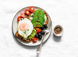 Delicious brunch - fried egg, avocado, grilled bread, dried olives, cherry tomatoes. Delicious healthy breakfast, snack on a light background, top view