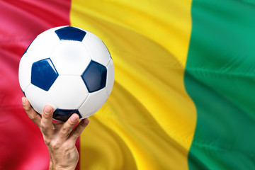 Guinea soccer concept. National team player hand holding soccer ball with country flag background....