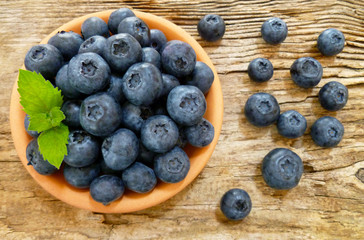 Bowl of fresh blueberries on rustic wooden old table. Freshly picked blueberries in bowl. Healthy organic fruit background. Organic food raw blueberries and mint leaf for healthy lifestyle.