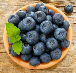 Bowl of fresh blueberries on rustic wooden old table. Freshly picked blueberries in bowl. Healthy organic fruit background. Organic food raw blueberries and mint leaf for healthy lifestyle.