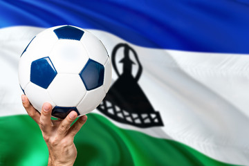 Lesotho soccer concept. National team player hand holding soccer ball with country flag background....
