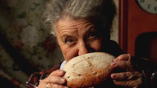 Elderly woman eating a big bun and smile on a dark background