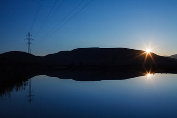 Power line in mountains and sunset reflected in a calm lake
