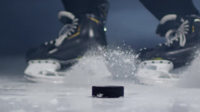 Extreme close up feet of unrecognizable ice hockey player hitting puck with stick during game