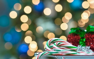 Candy canes on a plate with red gift box behind it and bokeh Christmas tree lights in the background. Christmas card festive image with room for text.