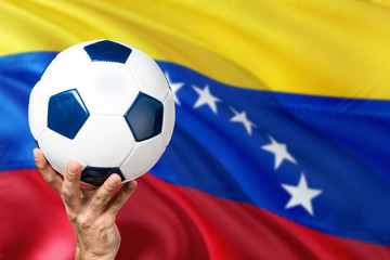 Fototapeta premium Venezuela soccer concept. National team player hand holding soccer ball with country flag background. Copy space for text.